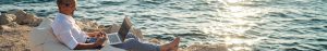 Businessperson sat on the beach using a laptop