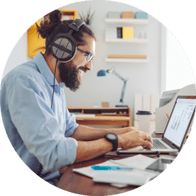 Man sat at a computer at home wearing headphones and smiling