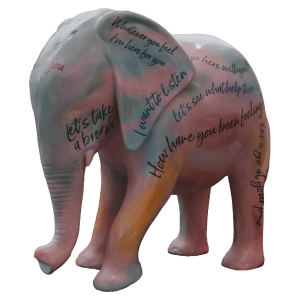 Elephant statue painted in shades of pink, blue, and green with mental health slogans written all over the statue