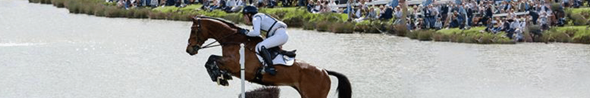 Field Talk Roadshow 8 Horse and rider leaping over a jump in front of a river. On the opposite bank, a crowd looks on